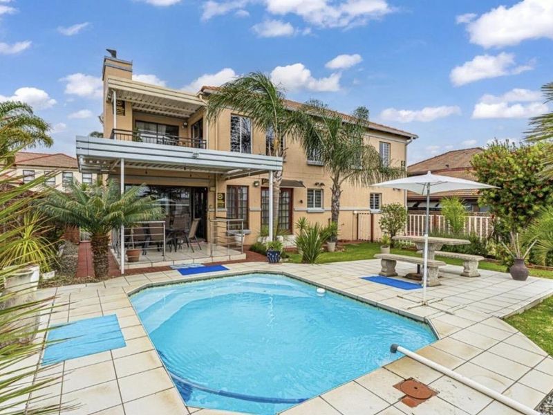 Rear view of a two-story house featuring a swimming pool, paved pool deck, covered patio area, and an upper-level balcony.