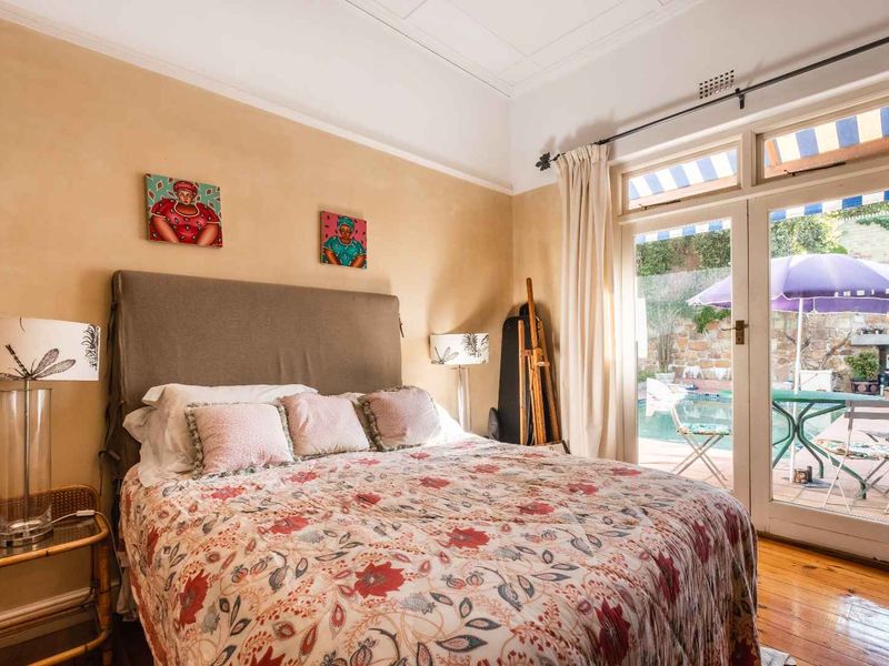 A bright bedroom featuring hardwood flooring and classic french doors that open directly onto a private patio and pool area.
