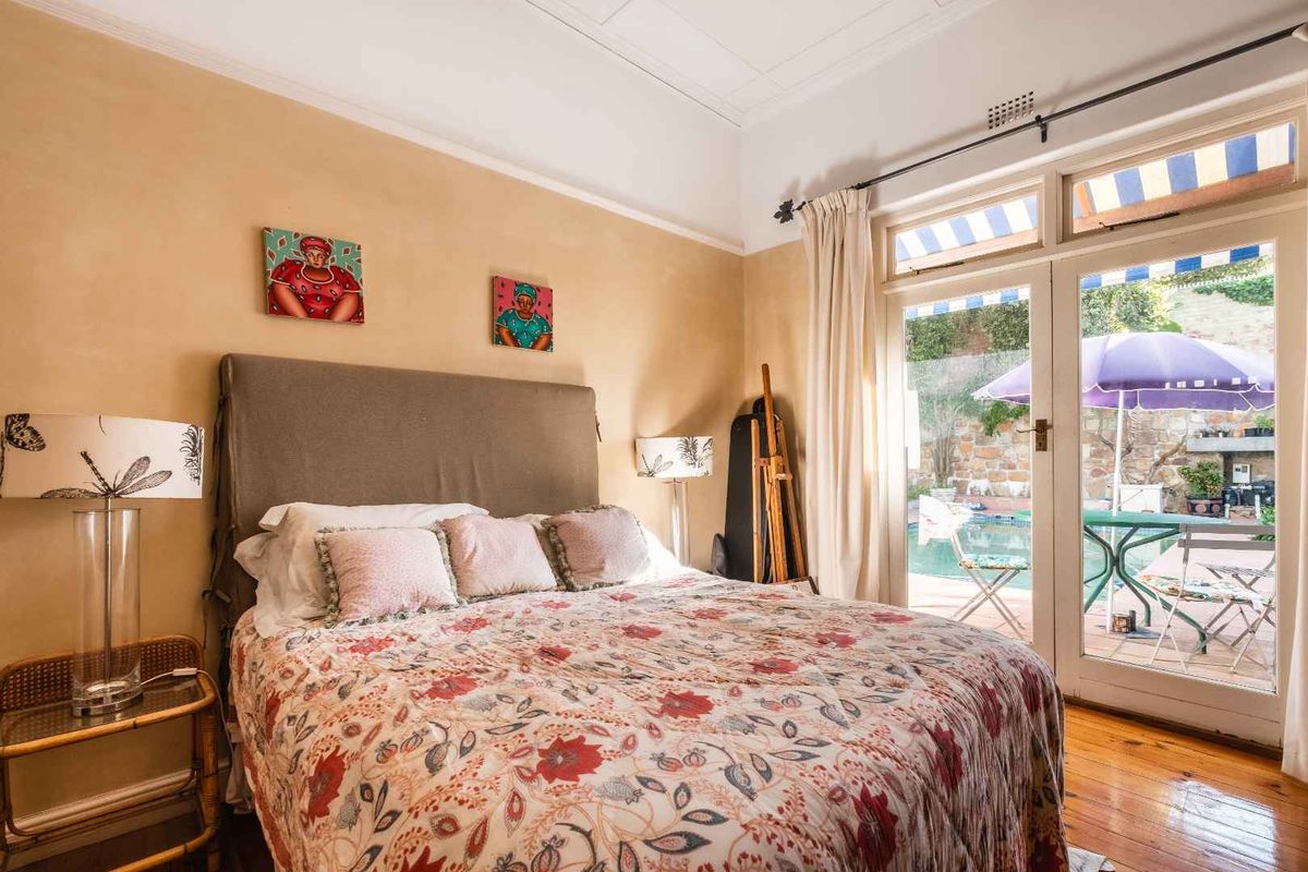A bright bedroom featuring hardwood flooring and classic french doors that open directly onto a private patio and pool area.