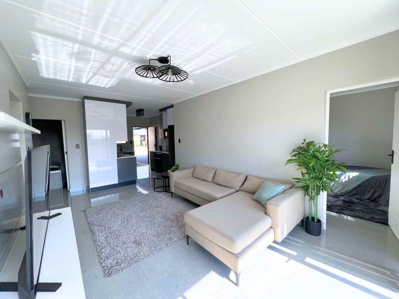 Modern open-plan living area featuring sleek glossy kitchen cabinetry, neutral wall tones, and polished tiled flooring throughout the space.