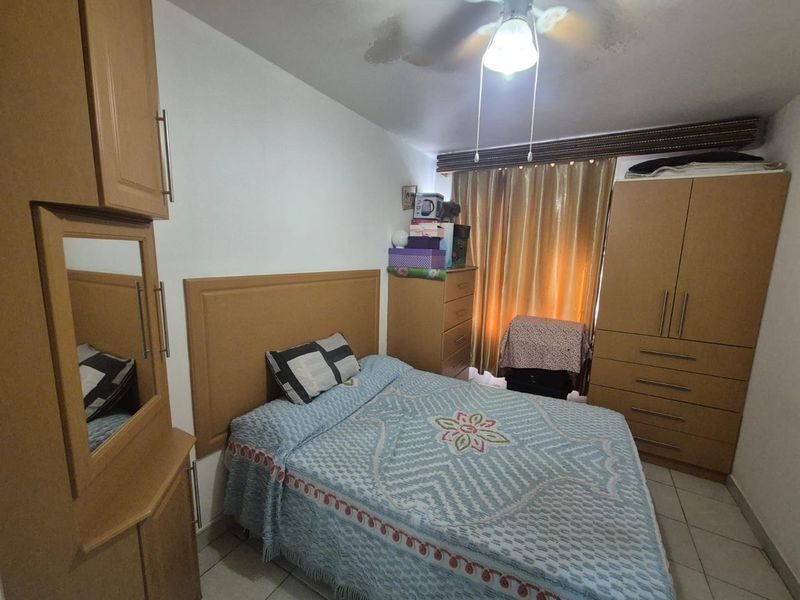 A compact bedroom featuring built-in wooden cabinetry, tiled flooring, and a ceiling fan. The room shows signs of water damage on the ceiling.