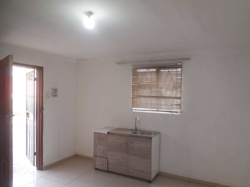 A compact, empty kitchen area featuring basic base cabinetry, a single sink, tiled flooring, and natural light through a window with venetian blinds.