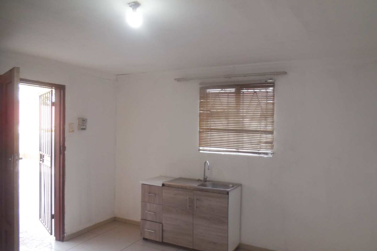 A compact, empty kitchen area featuring basic base cabinetry, a single sink, tiled flooring, and natural light through a window with venetian blinds.