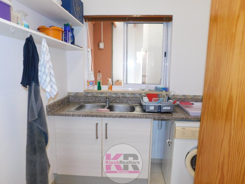 Functional scullery area featuring a double bowl stainless steel sink, granite countertops, built-in cabinetry, and open shelving for convenient storage and utility use.