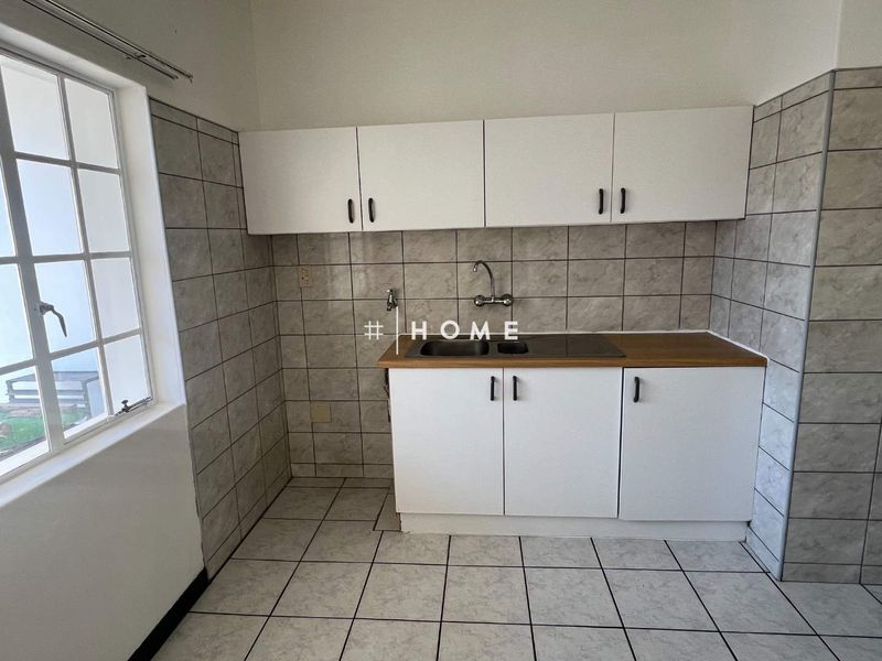 A functional scullery area featuring built-in cabinetry, a double basin sink, tiled splashbacks, and tiled flooring.