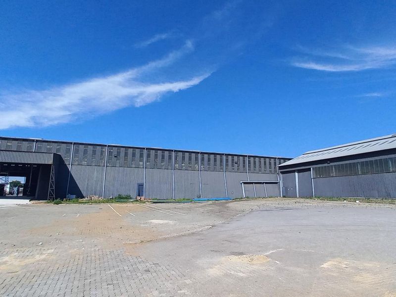 Wide-angle view of an industrial warehouse facility featuring extensive corrugated metal cladding and a large paved yard area.