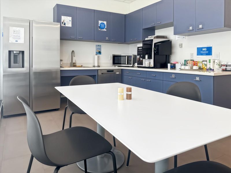 A functional office kitchen area featuring blue cabinetry, stainless steel appliances, and a clean, modern layout suitable for staff use.