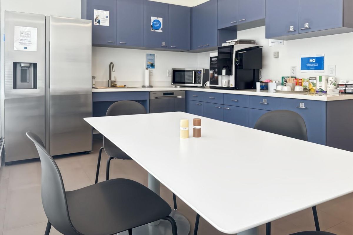 A functional office kitchen area featuring blue cabinetry, stainless steel appliances, and a clean, modern layout suitable for staff use.