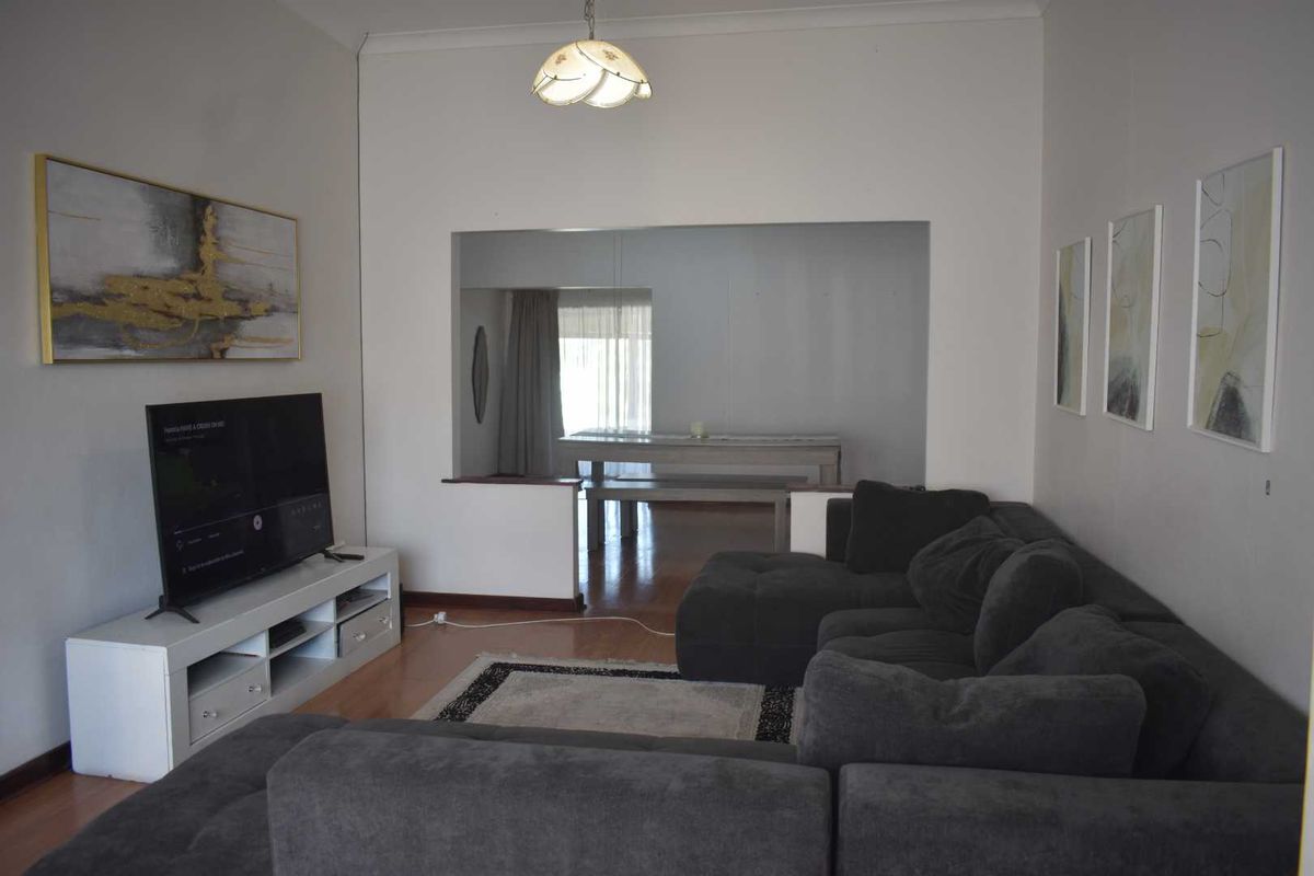 A living room featuring laminate flooring and a pass-through opening connecting to the adjacent dining area.
