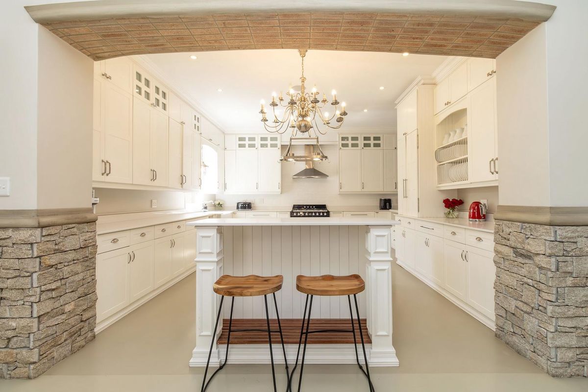 A well-appointed kitchen featuring white cabinetry, a central island, stone-clad archway detailing, and integrated stainless steel appliances.