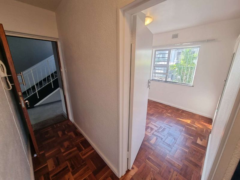 A bright hallway featuring classic parquet flooring, leading into an adjacent room with security bars on the window.