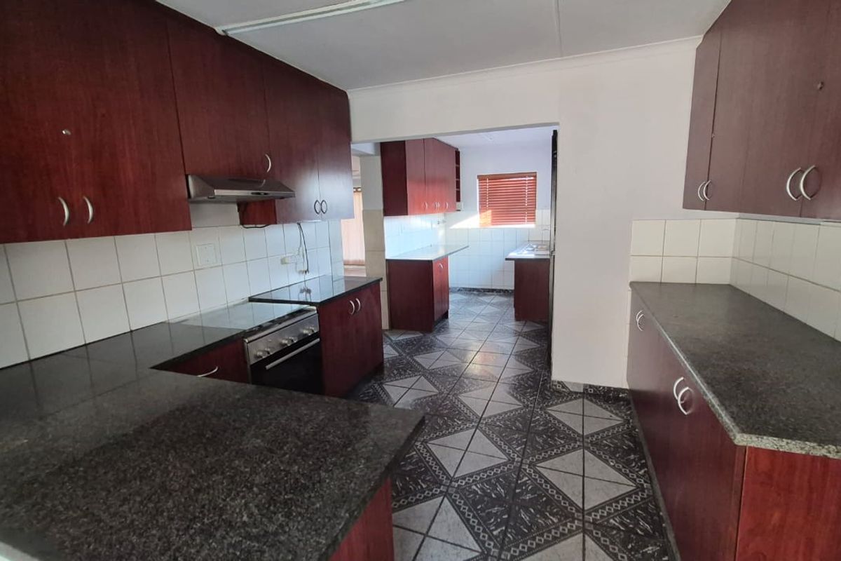 A spacious, empty kitchen featuring dark wood cabinetry, granite countertops, an integrated stove with extractor fan, and tiled flooring throughout.