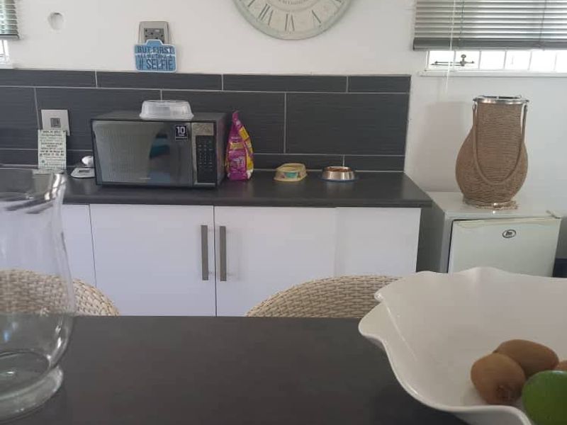 A functional kitchen area featuring white cabinetry, dark countertops, and a dark tiled splashback, complemented by venetian blinds.