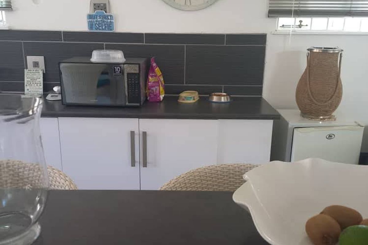A functional kitchen area featuring white cabinetry, dark countertops, and a dark tiled splashback, complemented by venetian blinds.