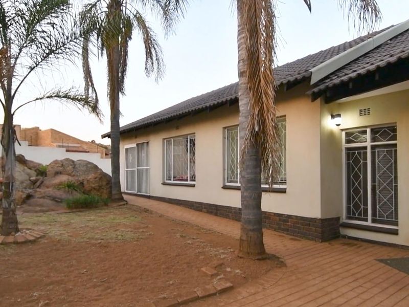 Rear view of the house featuring a paved walkway, security-fitted windows, and a landscaped garden area with mature palm trees.