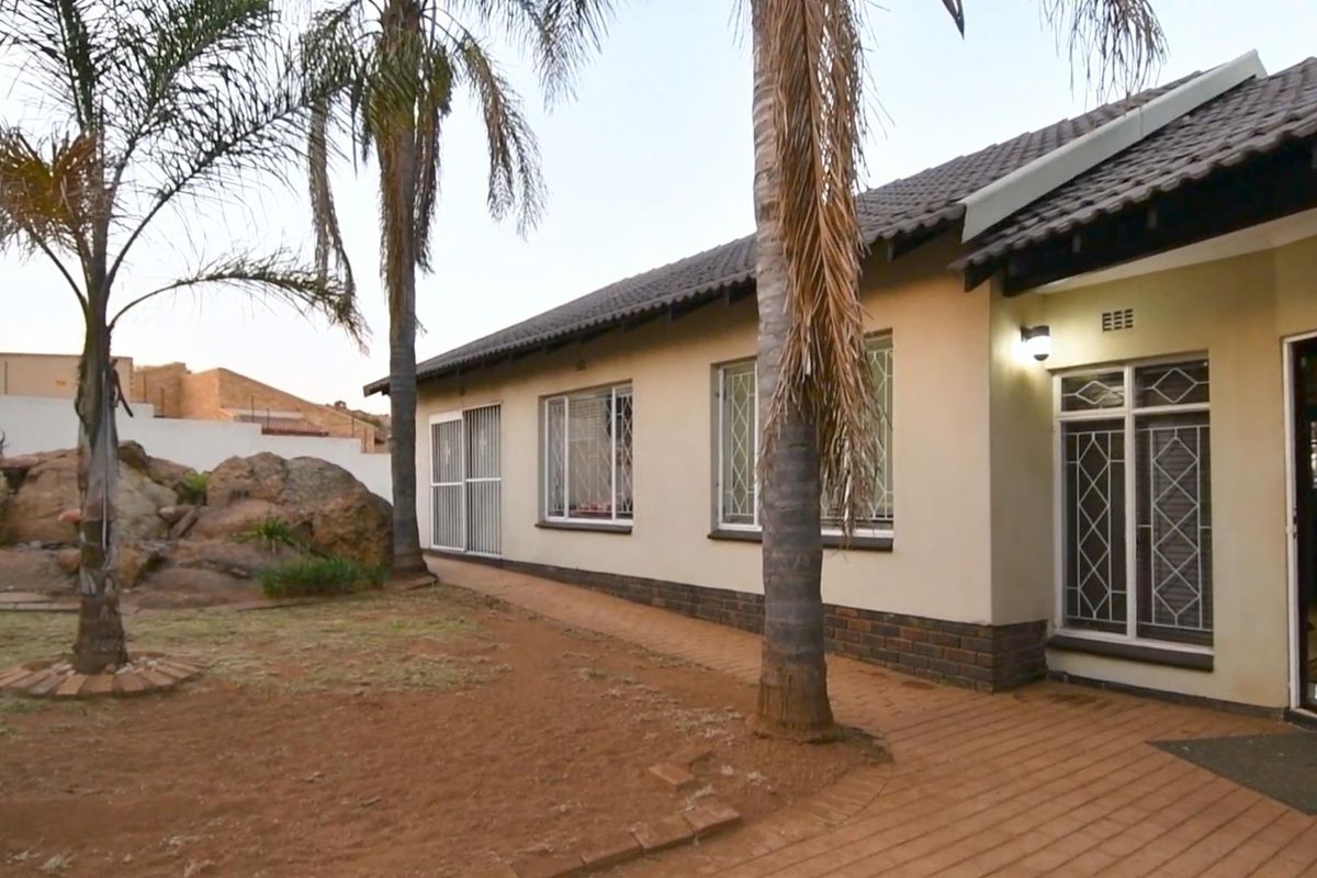 Rear view of the house featuring a paved walkway, security-fitted windows, and a landscaped garden area with mature palm trees.