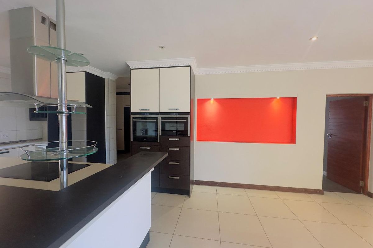 Modern kitchen featuring a breakfast bar, built-in double ovens, integrated cabinetry, and a decorative recessed wall niche with accent lighting.