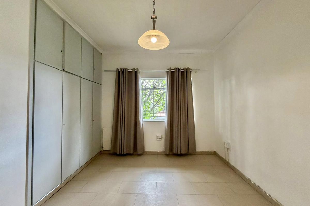 A bright, empty bedroom featuring built-in floor-to-ceiling cupboards, tiled flooring, and a central pendant light fixture.