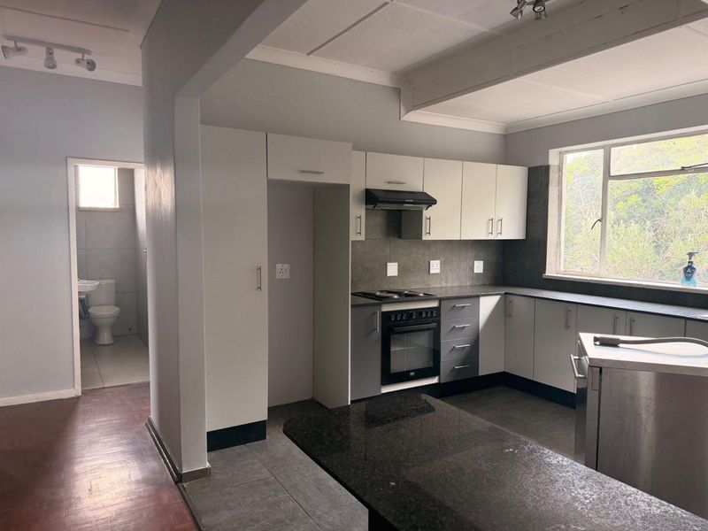 A functional kitchen featuring built-in cabinetry, granite countertops, and integrated appliances, with an adjacent view into a tiled bathroom area.
