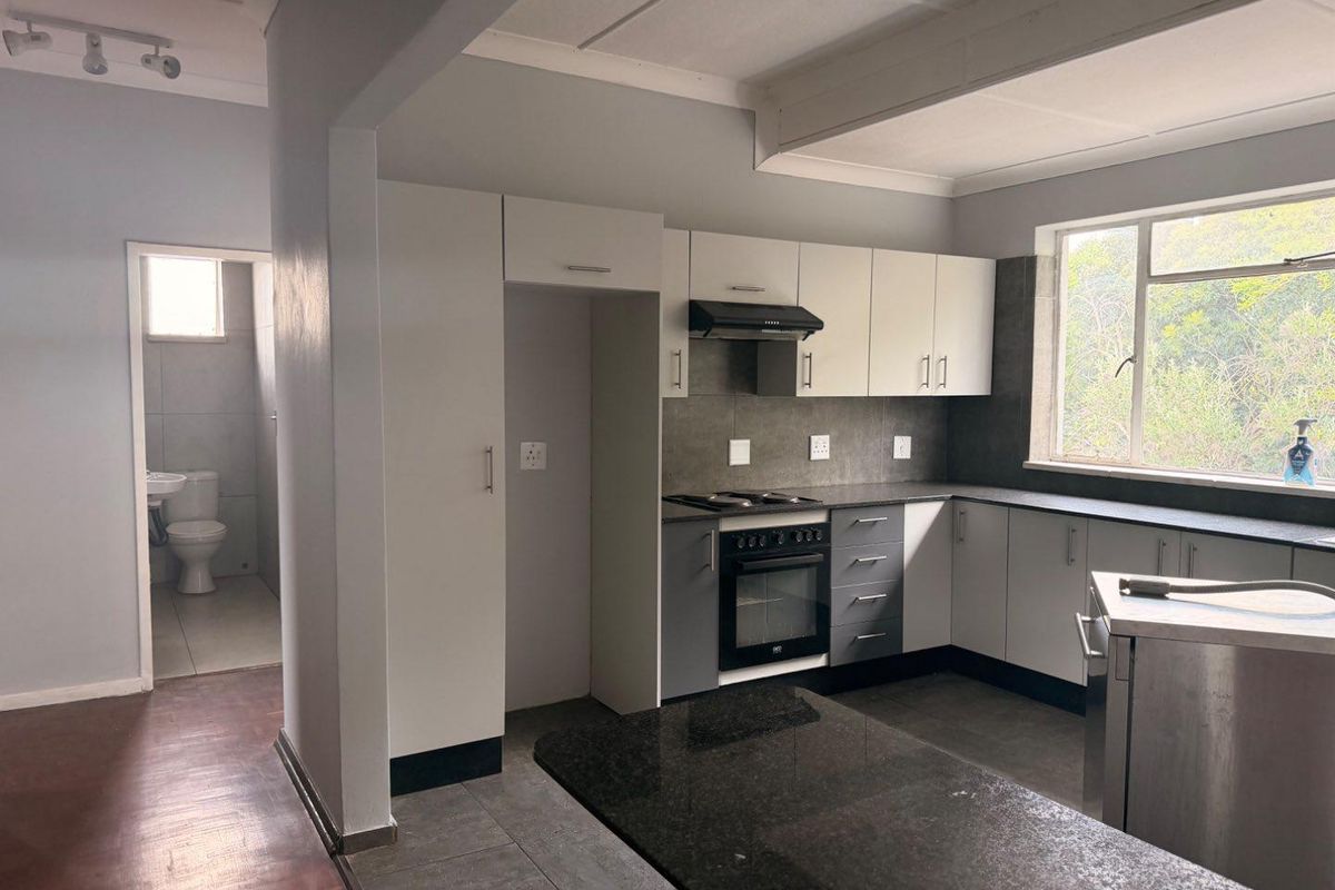 A functional kitchen featuring built-in cabinetry, granite countertops, and integrated appliances, with an adjacent view into a tiled bathroom area.