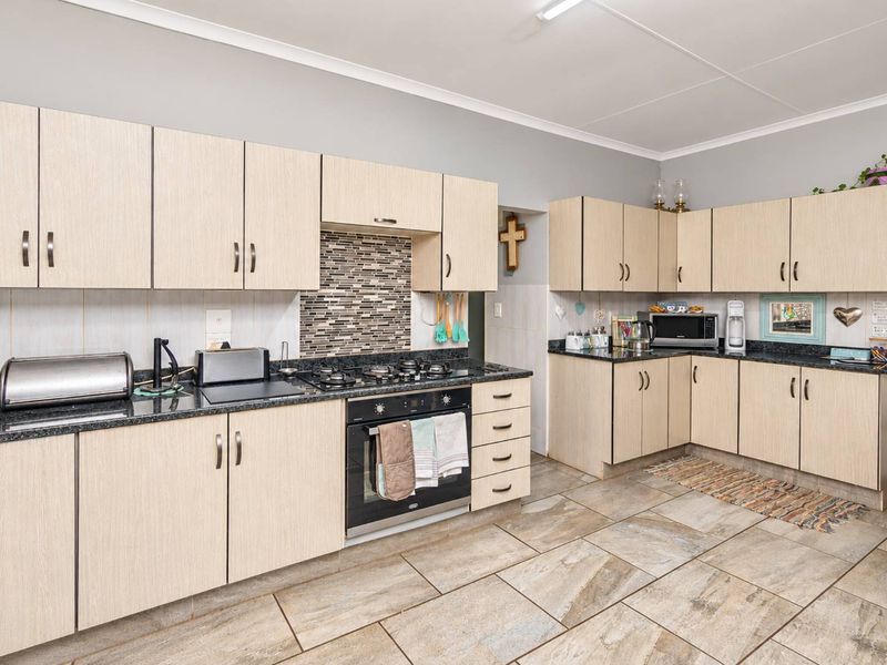 A functional kitchen featuring light wood-grain cabinetry, dark granite countertops, a gas hob, built-in oven, and durable tiled flooring.