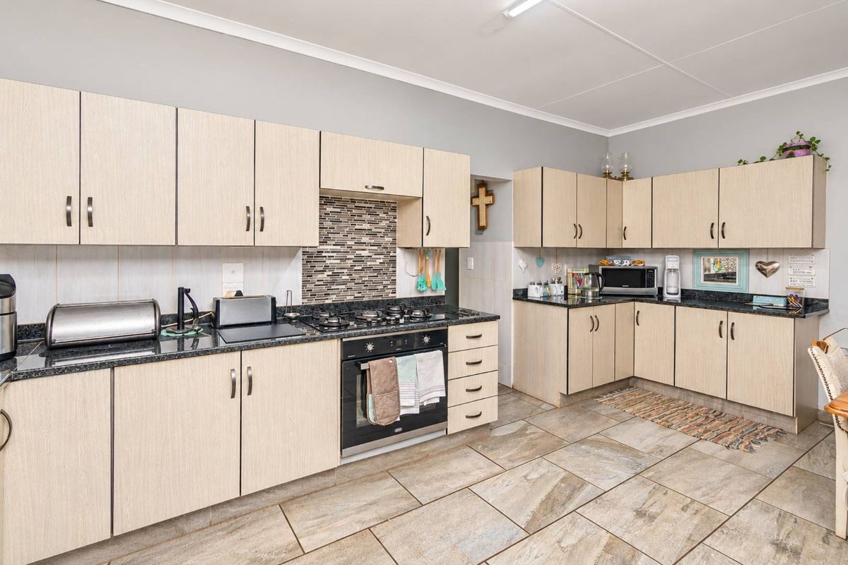 A functional kitchen featuring light wood-grain cabinetry, dark granite countertops, a gas hob, built-in oven, and durable tiled flooring.