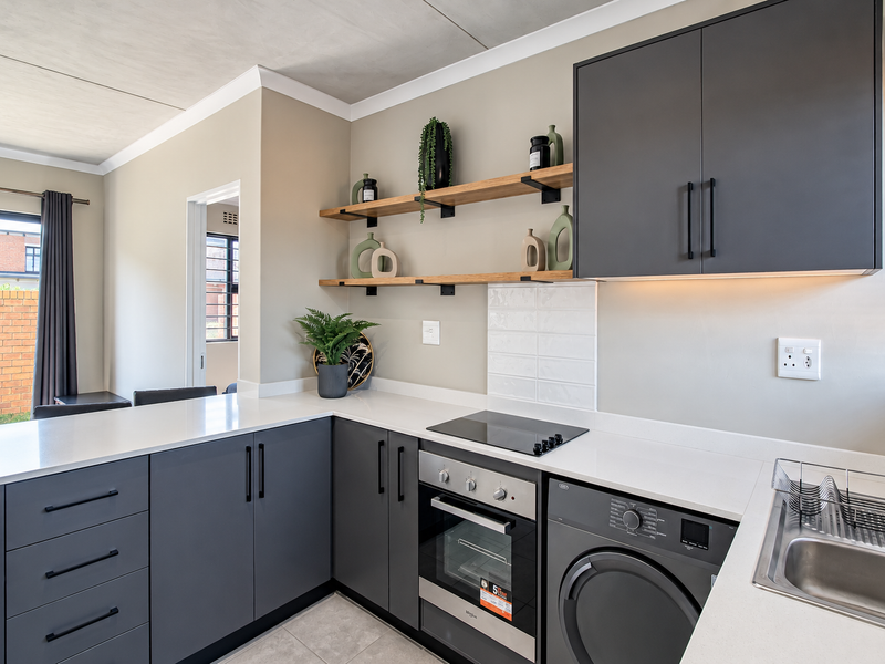 Modern kitchen featuring dark grey cabinetry, stone countertops, built-in oven, electric hob, and floating timber shelving with integrated under-cabinet lighting.