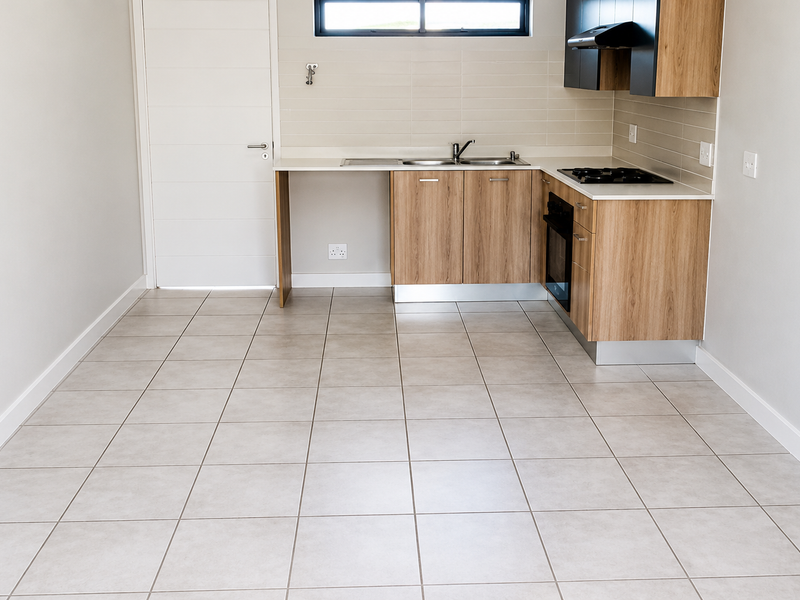 A clean, modern, and empty kitchen featuring wood-finish cabinetry, built-in oven, gas hob, and neutral tiled flooring.