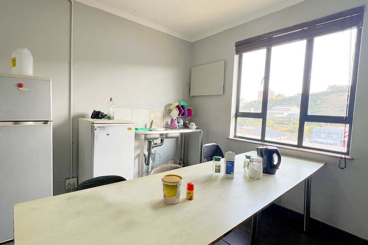 A functional industrial kitchenette area featuring a stainless steel sink, tiled flooring, and large windows providing natural light.