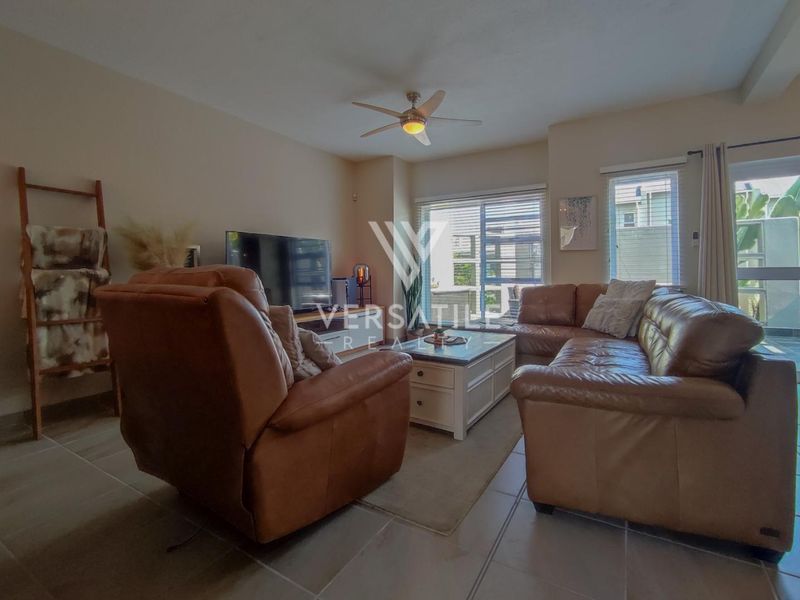 A comfortable living room featuring tiled flooring, a ceiling fan, and large sliding glass doors providing natural light and access to the outdoor area.