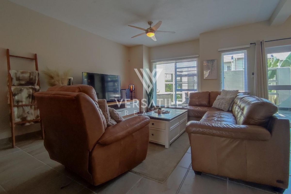 A comfortable living room featuring tiled flooring, a ceiling fan, and large sliding glass doors providing natural light and access to the outdoor area.
