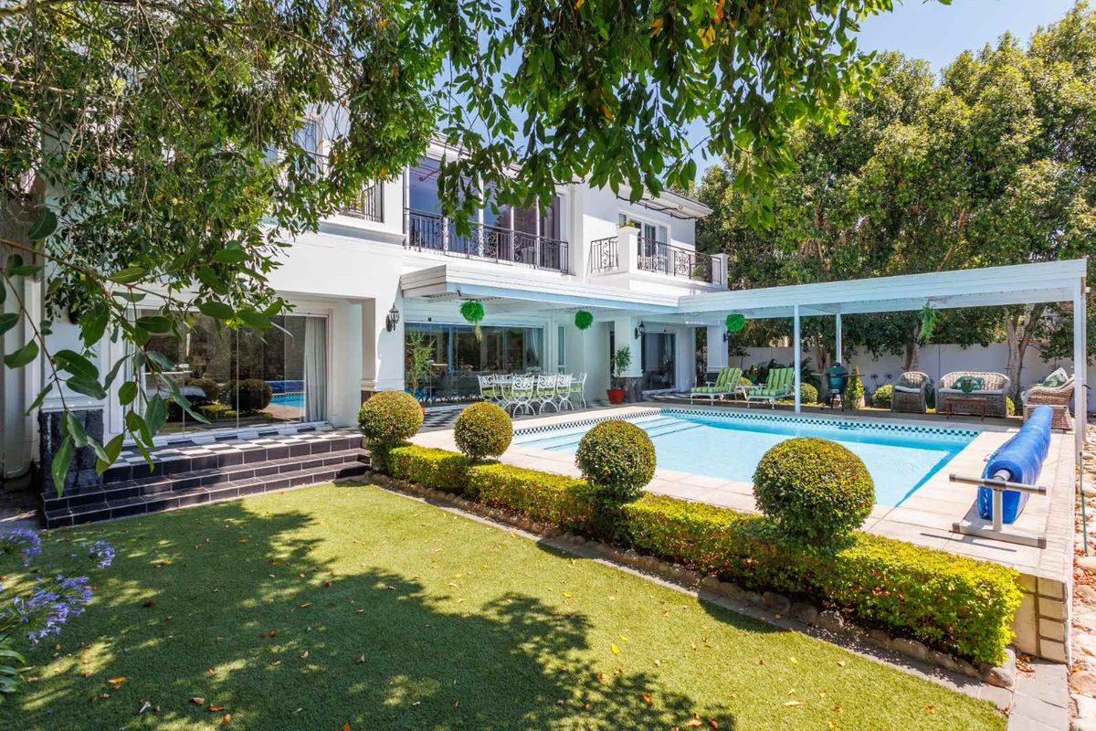 Rear view of the property featuring a swimming pool, covered patio area, landscaped garden, and upper-level balconies with wrought iron railings.