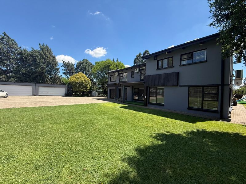 Spacious rear exterior view featuring a large manicured lawn, paved driveway, and a double garage attached to the modern two-story residential building.