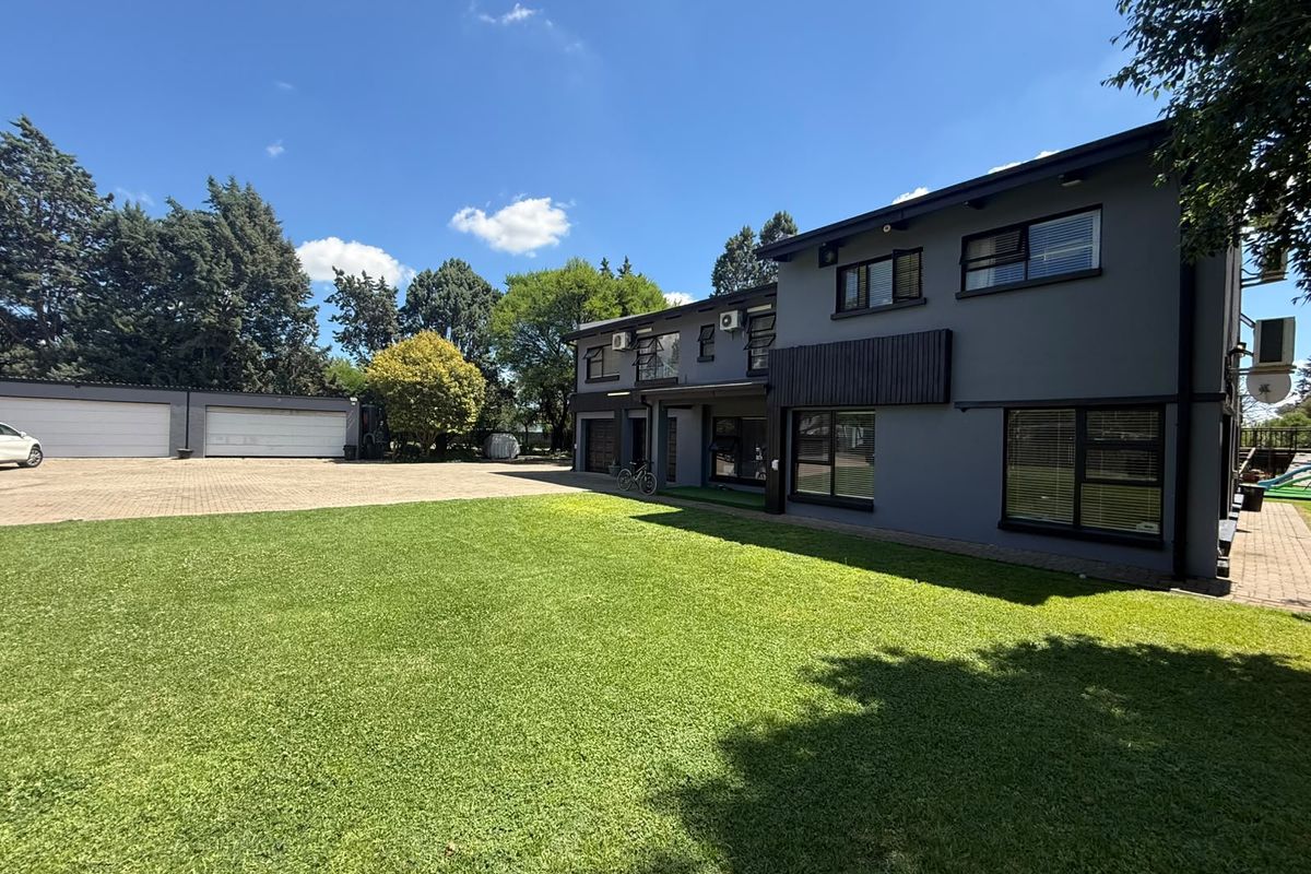 Spacious rear exterior view featuring a large manicured lawn, paved driveway, and a double garage attached to the modern two-story residential building.