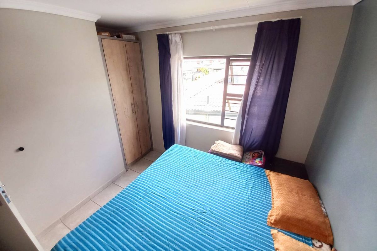 A functional bedroom featuring a built-in wardrobe, tiled flooring, and a window providing natural light.