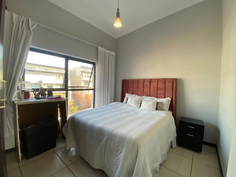 A functional bedroom featuring tiled flooring, a large window providing natural light, and a simple pendant light fixture.