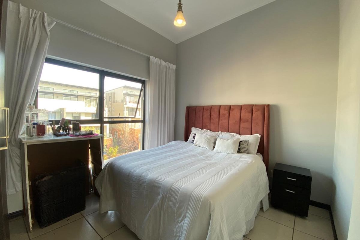 A functional bedroom featuring tiled flooring, a large window providing natural light, and a simple pendant light fixture.