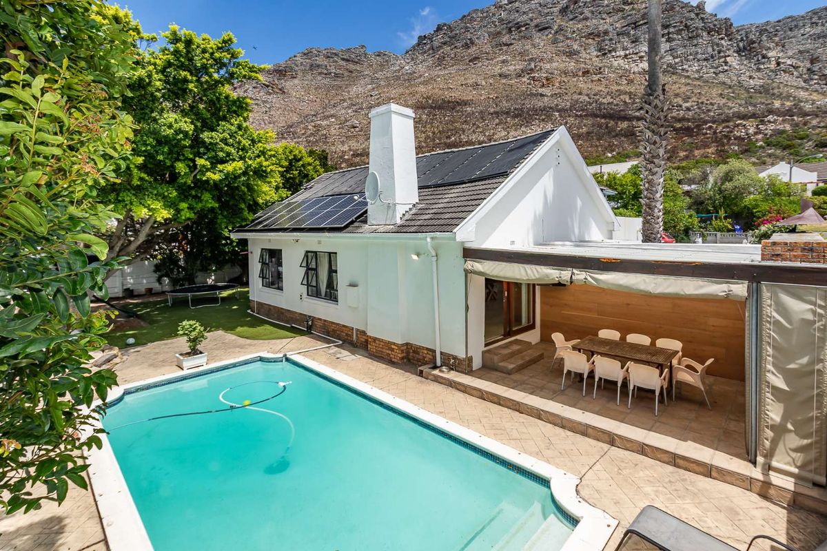 Rear exterior view featuring a swimming pool, covered patio area, and roof-mounted solar panels set against a mountain backdrop.