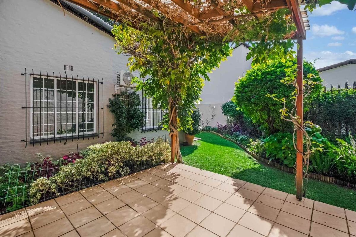 A private rear garden featuring a tiled patio area, a timber pergola with climbing vines, and a well-maintained lawn.