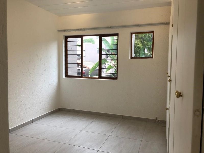 A vacant bedroom featuring tiled flooring, built-in cupboards, and security bars on the windows, offering a clean and neutral space ready for personalization.