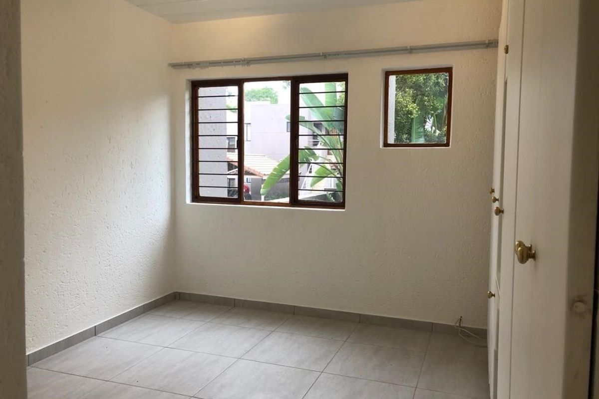 A vacant bedroom featuring tiled flooring, built-in cupboards, and security bars on the windows, offering a clean and neutral space ready for personalization.