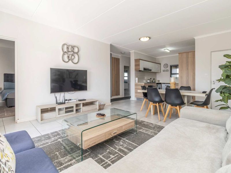 An open-plan living and dining area featuring tiled floors, neutral walls, and a functional kitchen with built-in cabinetry and integrated appliances.