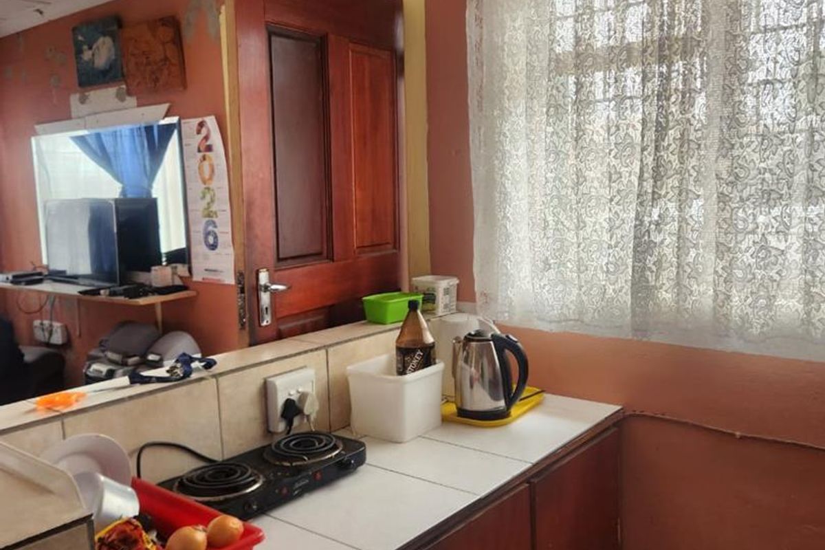 A compact kitchen area featuring wooden cabinetry, a tiled countertop, and an electric hob, showing signs of age and wear.