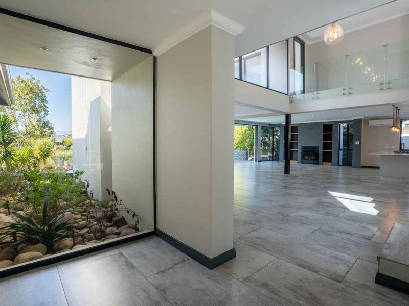 Spacious open-plan living area featuring large format floor tiles, a double-volume ceiling, glass balustrades, and a unique internal courtyard garden.