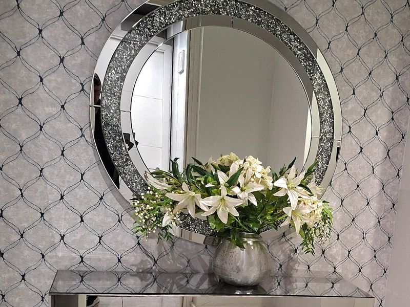 A close-up view of a decorative wall featuring patterned wallpaper and a large circular mirror.