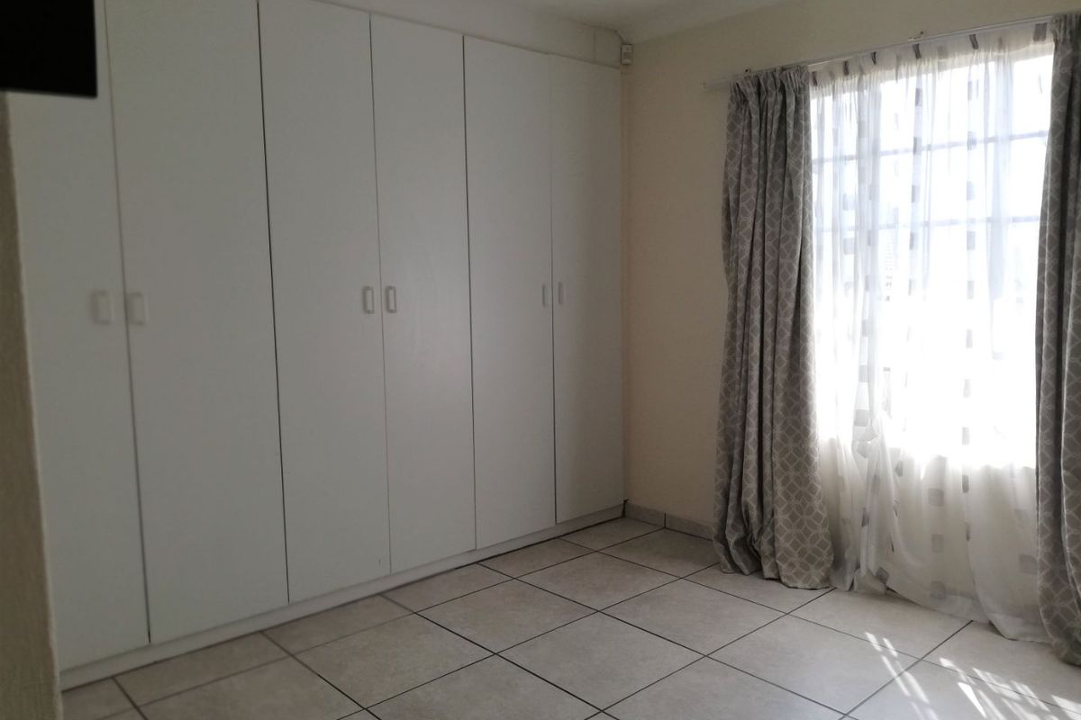 A bright, empty bedroom featuring neutral tiled flooring and extensive built-in cupboard storage, offering a clean and versatile space.