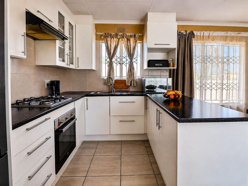 A well-maintained kitchen featuring white cabinetry, dark countertops, a gas hob, an electric oven, and tiled flooring with direct access to the exterior.