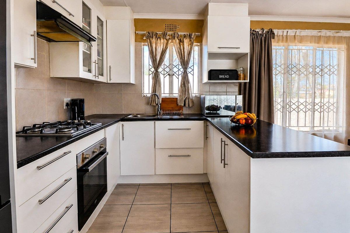 A well-maintained kitchen featuring white cabinetry, dark countertops, a gas hob, an electric oven, and tiled flooring with direct access to the exterior.