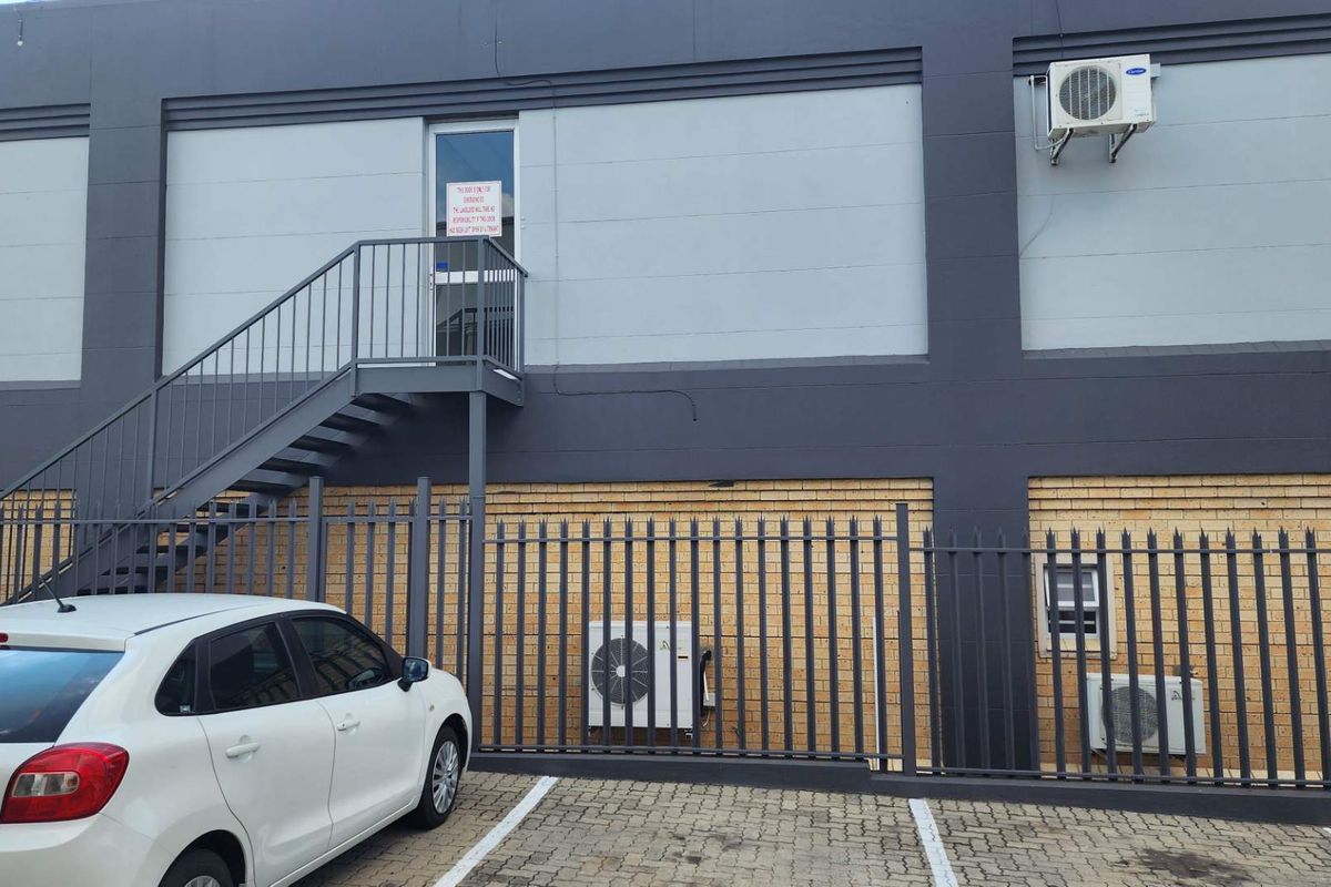 Exterior view of a commercial building featuring a metal staircase, security fencing, and multiple wall-mounted air conditioning units.
