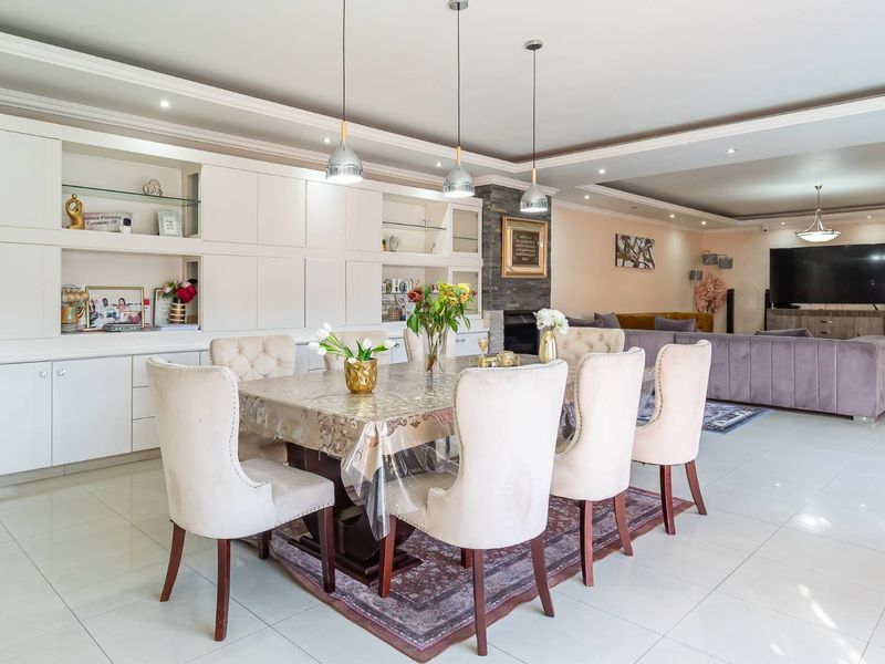 Spacious open-plan living and dining area featuring built-in cabinetry, a stone-clad fireplace, recessed ceiling details, and polished tiled flooring.